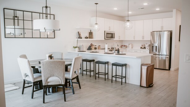 Una cocina moderna con armarios blancos, una isla central con taburetes de bar, un refrigerador de acero inoxidable e iluminación colgante.