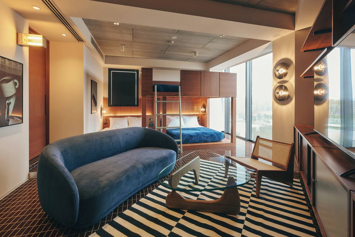 Una habitación de hotel moderna con una cama litera, un sofá azul, una mesa de centro de cristal y un piso a cuadros.