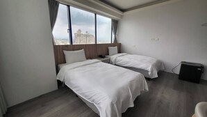 Quarto de hotel com duas camas, vista para o horizonte urbano e um pequeno alto-falante preto no chão.