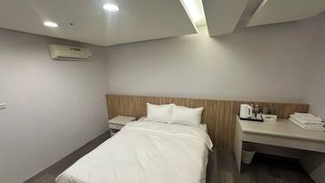 A hotel room with a bed, a bedside table, a desk with a chair, a lamp, and a small table with toiletries.