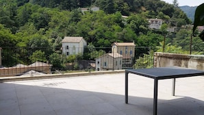 A terrace with a table, surrounded by a fence and trees. - Villa Denise (Vals-les-Bains)