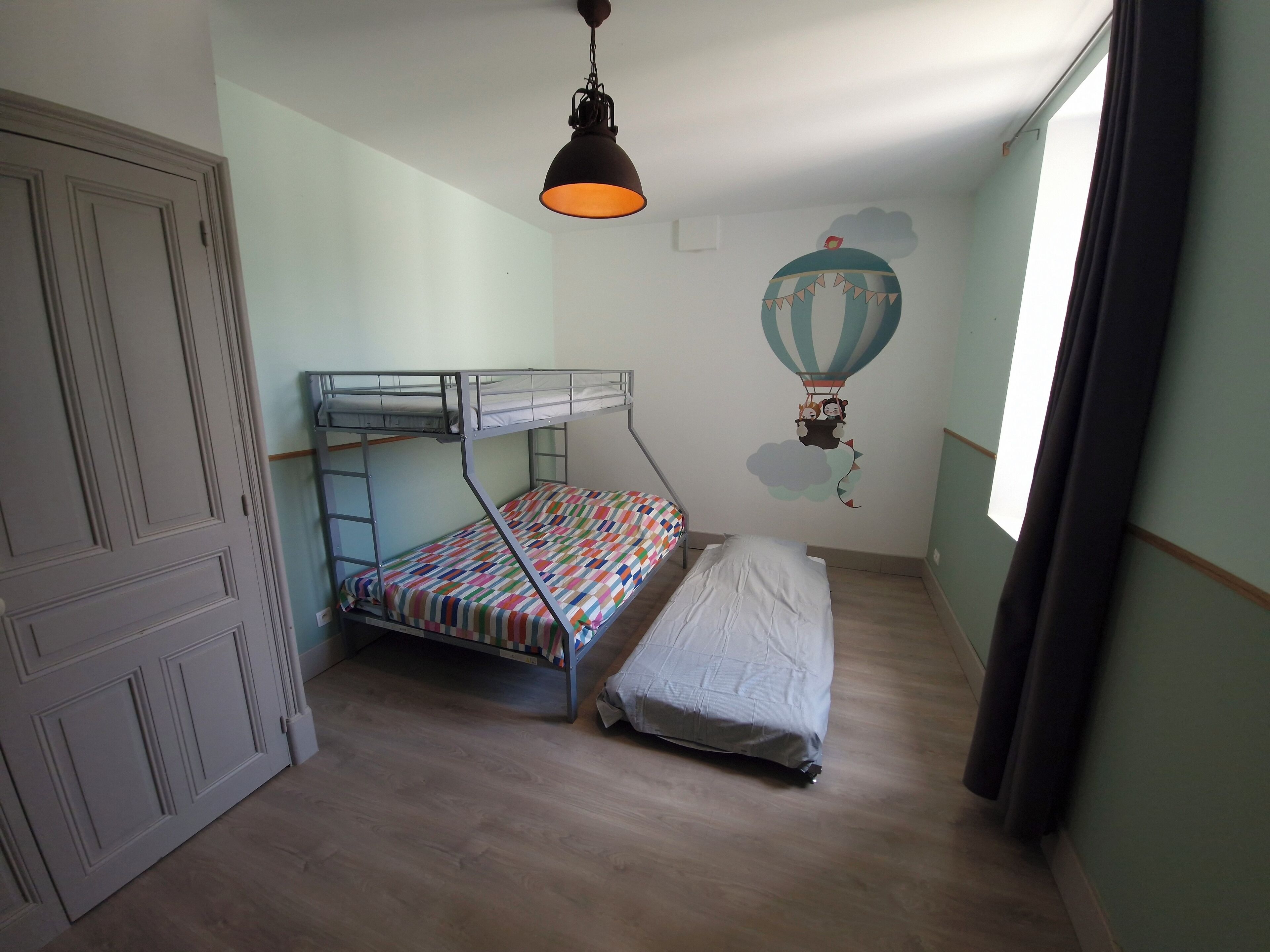 A room with a bunk bed, a wardrobe, a hanging light fixture, and a wall decoration.