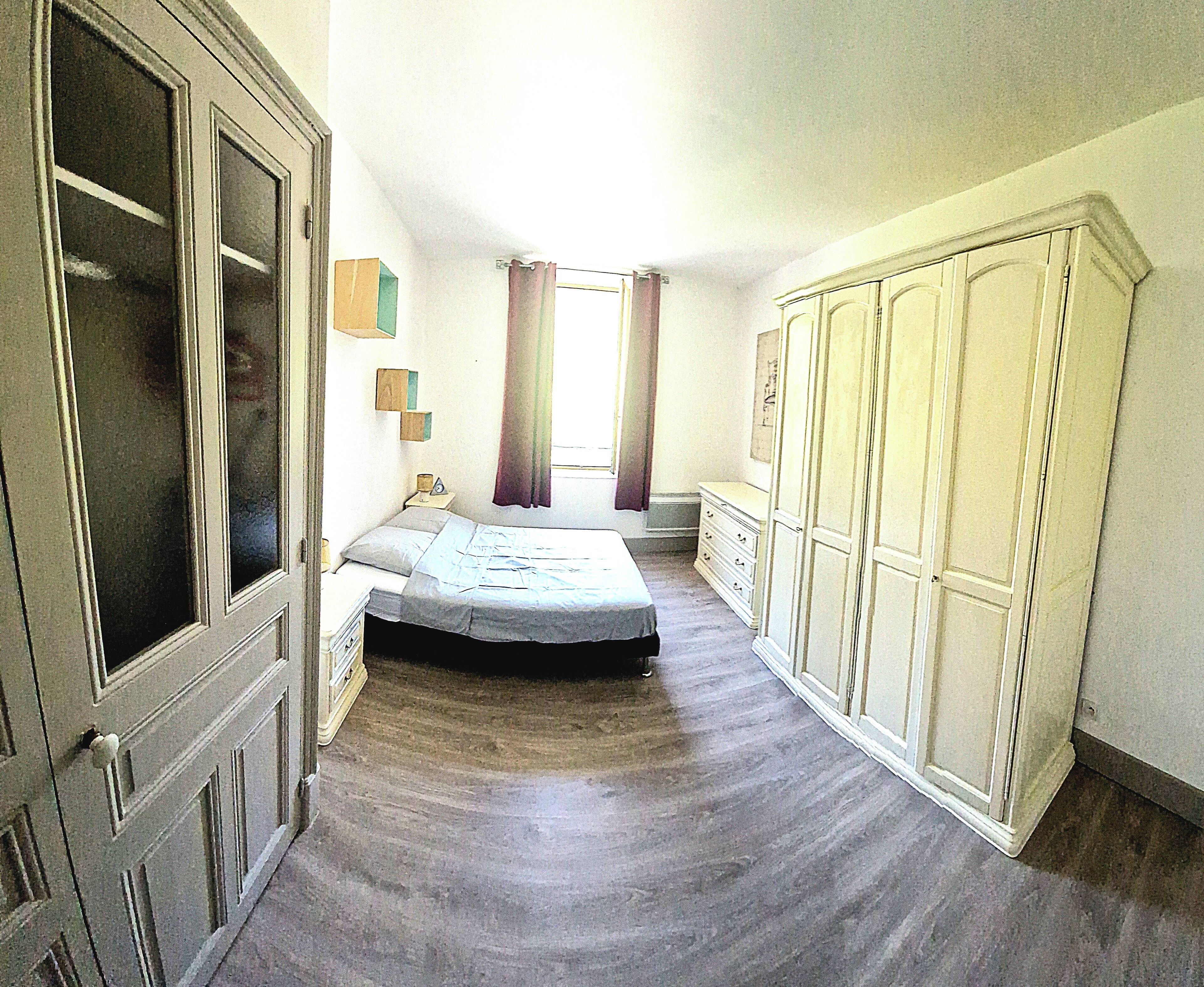 A bedroom with a bed, a wardrobe, a dresser, and a window with curtains.