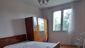 A bedroom with a wooden bed, a wardrobe, a chandelier, and a window with curtains. - Quiet, 70s-style house with large garden in the heart of the Lot et Garonne region (Saint-Étienne-de-Fougères)