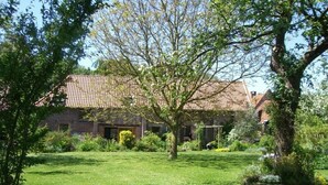 Een huis met pannendak, omringd door een verzorgd gazon en diverse bomen.