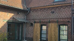 Een gebouw van baksteen met een pannendak, een groene deur en een raam met een luik.