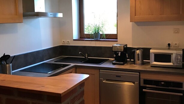 Een moderne keuken met een accentmuur van baksteen, roestvrijstalen apparatuur en een raam met natuurlijk licht.