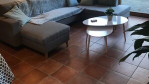 Een moderne woonkamer met een hoekbank, een kleine ronde tafel en een groot raam met gordijnen.