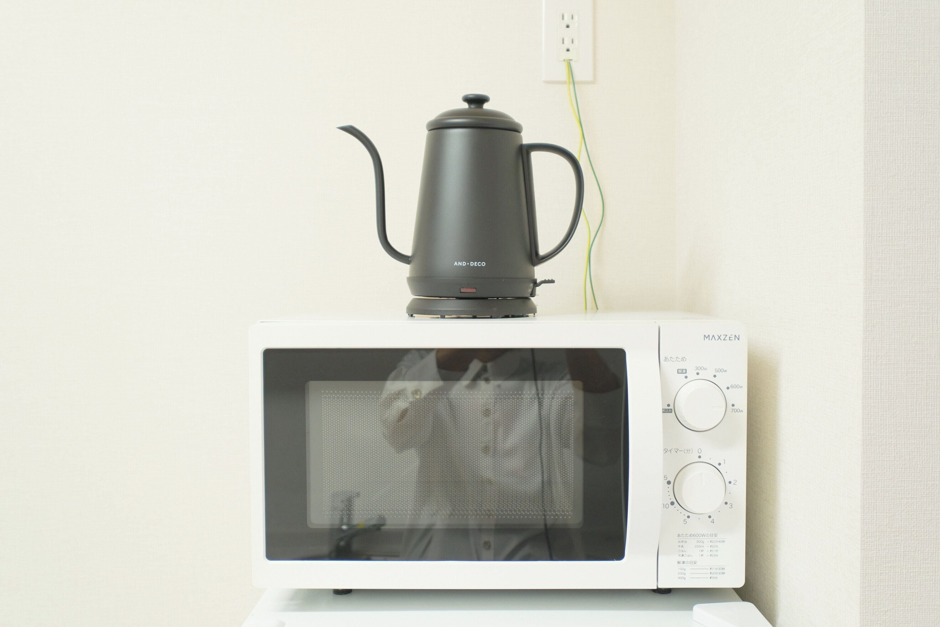 A white microwave oven with a black electric kettle on top.