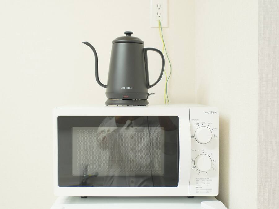 A white microwave oven with a black electric kettle on top.