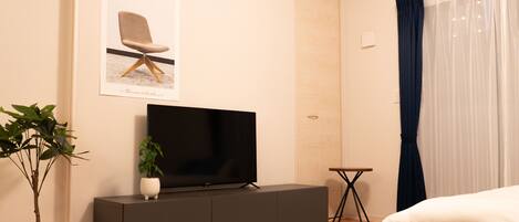 A modern bedroom with a bed, a TV on a cabinet, a potted plant, and a framed picture on the wall.