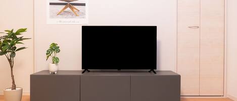 A modern living room with a flat-screen TV on a dark grey cabinet, a light-colored rug, and a potted plant.