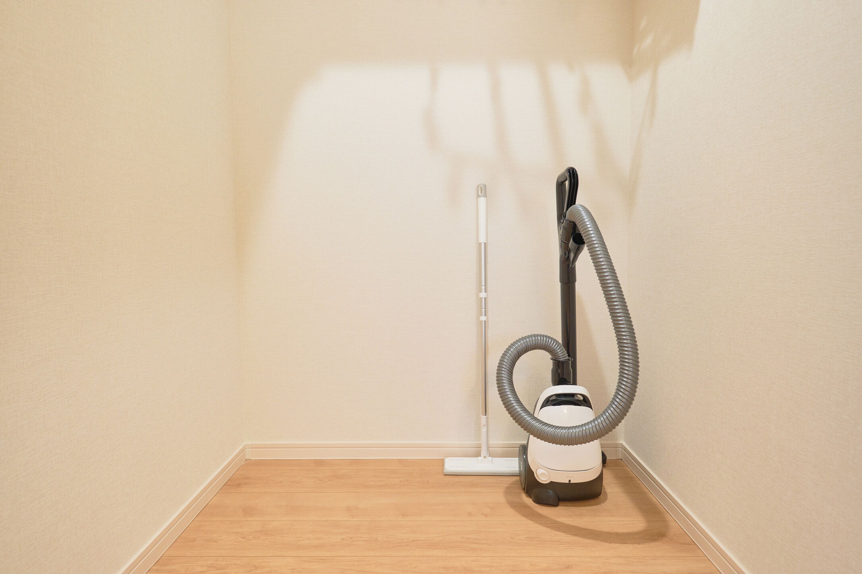 A corner of a room with a vacuum cleaner and a broom.