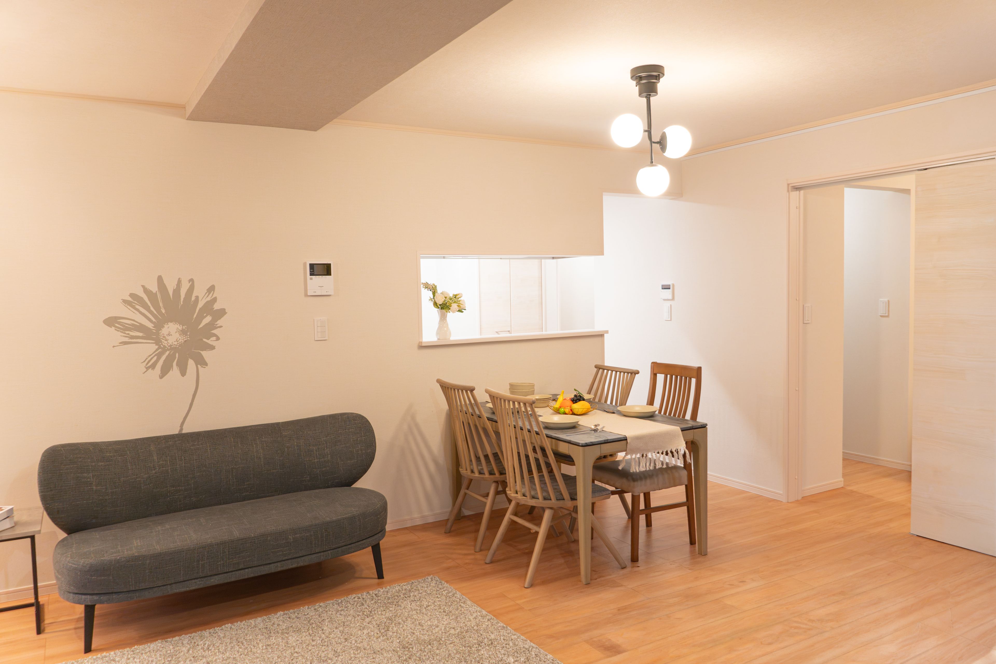 Una sala de estar moderna con un sofá gris, una mesa de comedor de madera con sillas, una alfombra pequeña y un aplique de techo.