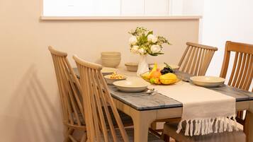 A dining table with four wooden chairs, a vase with flowers, and a fruit basket.