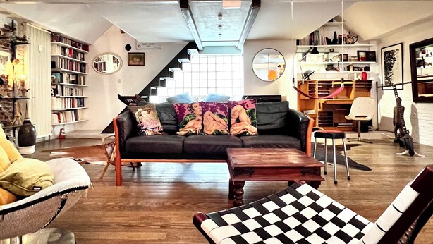 A spacious loft with a high ceiling, a staircase leading to an upper level, a cozy seating area with a sofa and armchairs, and a dining area with a table and chairs. - Loft Atelier au Style Vintage (Brussels)