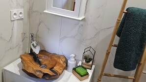A bathroom with a marble wall, a wooden vanity, a mirror, a towel rack, and a small plant.