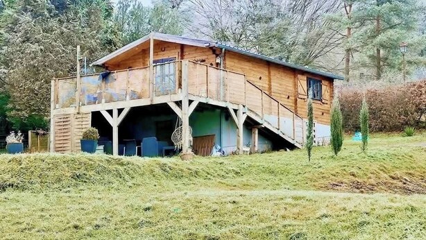 A wooden cabin with a balcony, a covered porch, and a small garden area.