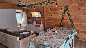 A cozy cabin interior with a sofa, a dining table, and a TV mounted on the wall.