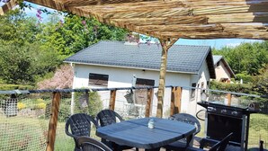 An outdoor patio with a wooden deck, a round table with chairs, and a barbecue grill.