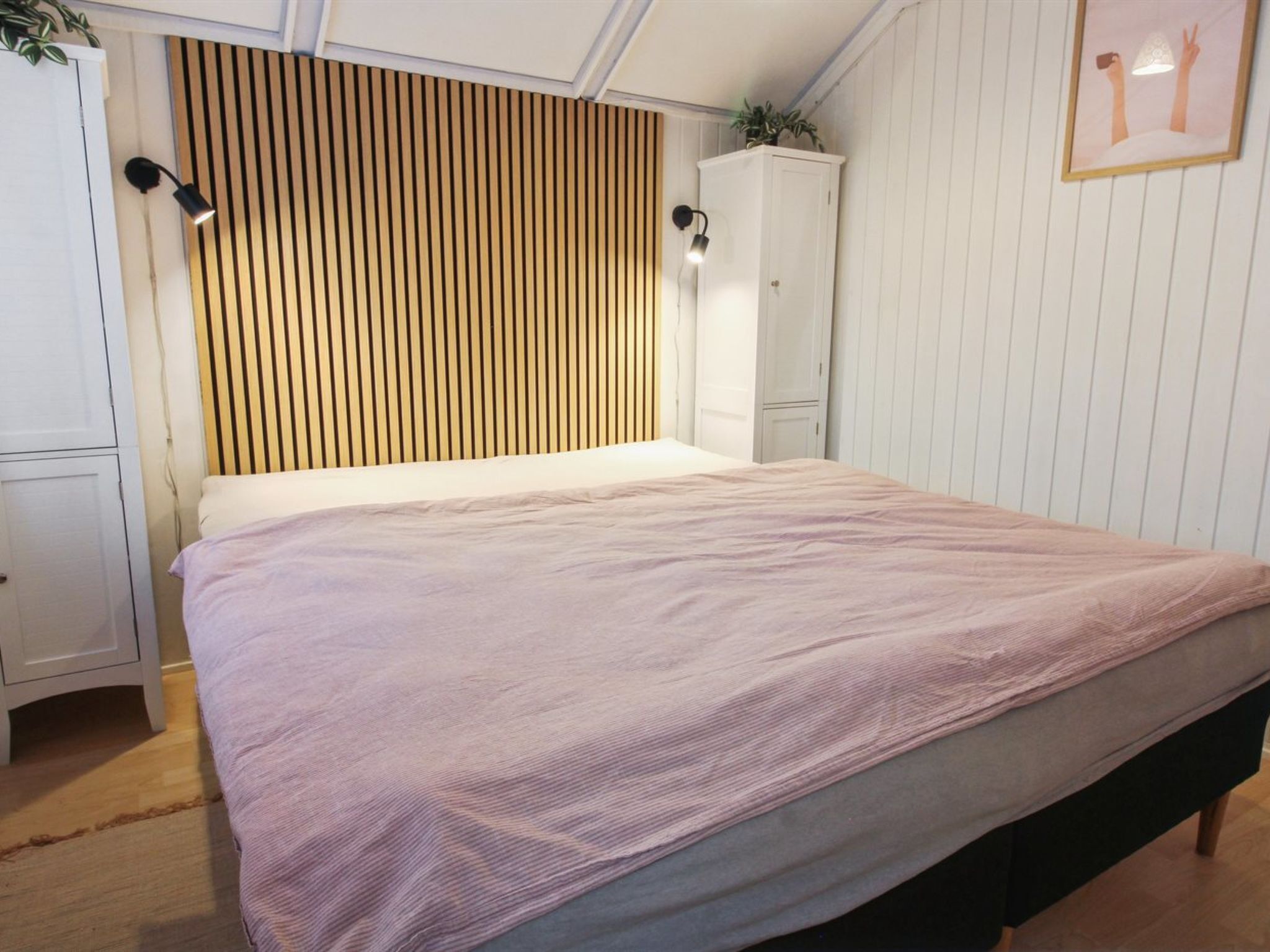 A bedroom with a bed, wooden slat headboard, white wardrobe, and a framed picture on the wall.