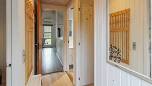 Um corredor com piso de madeira e paredes brancas, que leva a um quarto com janela e porta.