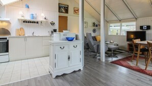 Cozinha moderna com armários brancos, forno embutido e área de refeições com televisão e assentos.