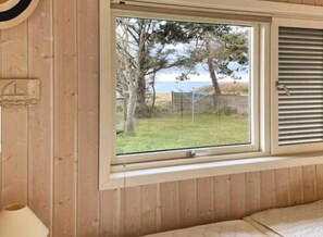 Ein Zimmer mit Holzwänden, einem Fenster mit Blick auf Bäume und einen Zaun, sowie einem Bett.