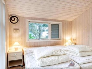 Une chambre Ă coucher comprenant un lit, deux tables de chevet, une fenĂȘtre avec volets et un luminaire fixĂ© au mur.