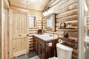 Baño de cabaña de madera con puerta de madera, un lavabo con espejo, un inodoro y una repisa con una planta.