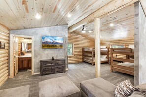 Interior de una cabaña de troncos con literas, un sofá gris, un aparador y un cuadro en la pared.