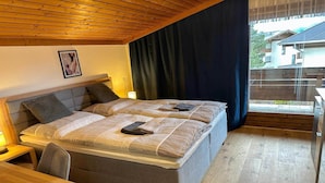 A double bed with a headboard, bedside tables, and a view of a residential area through a window. - Alpine Hideaway in Saalfelden (Saalfelden am Steinernen Meer)