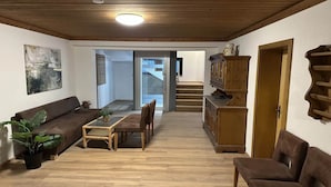 A spacious living area with a wooden ceiling, a brown sofa, a dining table with chairs, and a staircase leading to an upper floor. - Alpine Hideaway in Saalfelden (Saalfelden am Steinernen Meer)