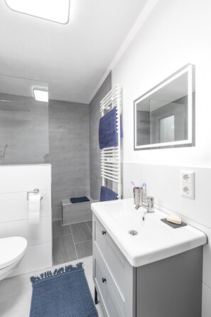 Uma casa de banho moderna com lavatório branco, espelho e barra de toalhas.