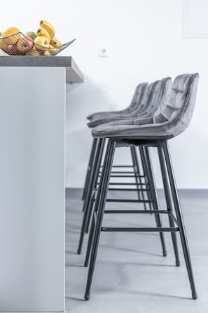 Una cocina moderna con una cesta de frutas en la encimera y una fila de taburetes de bar.