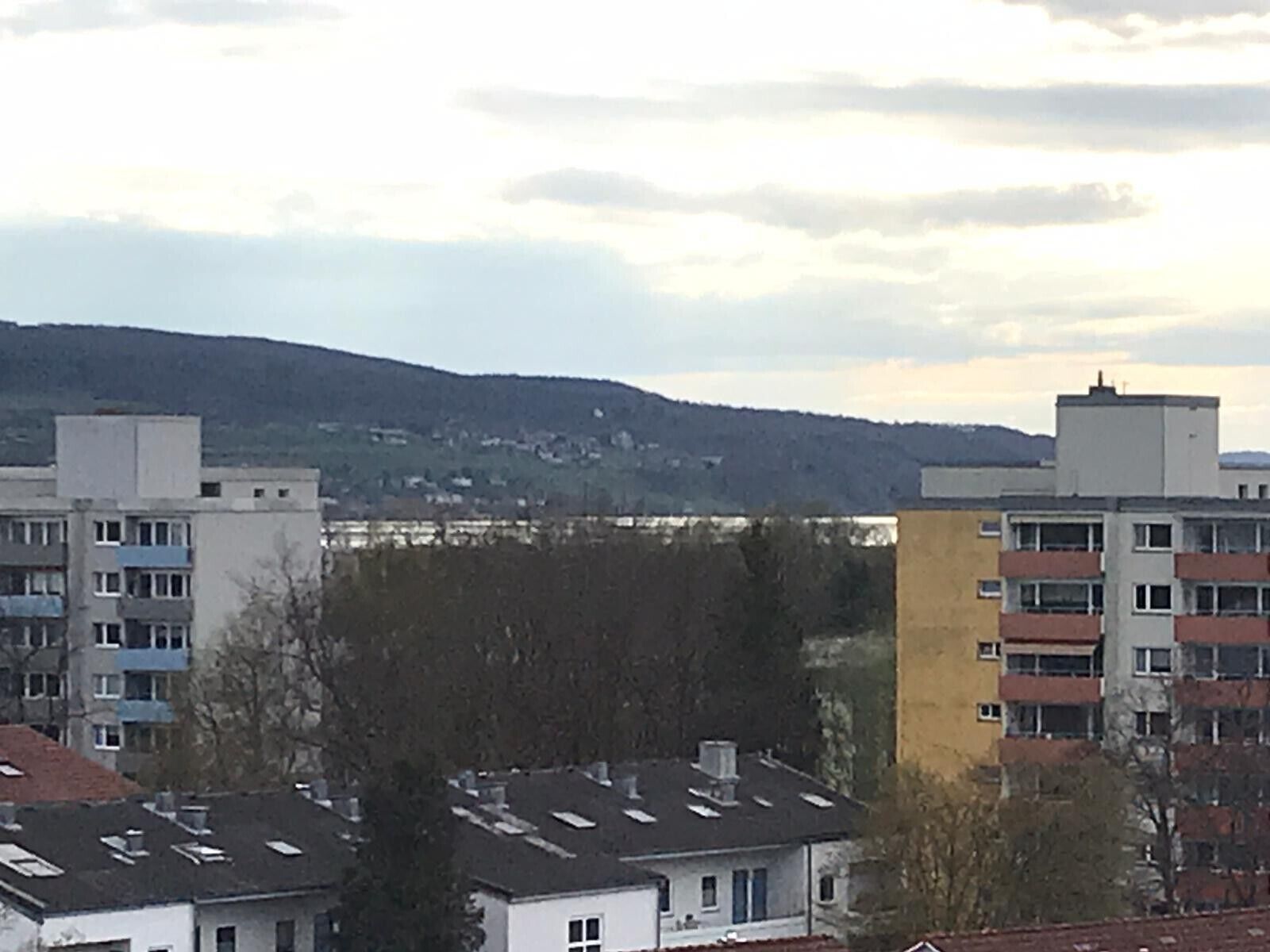 Een woonwijk met meerlaagsgebouwen, waarvan sommige balkons hebben, en een heuvelachtig landschap op de achtergrond.