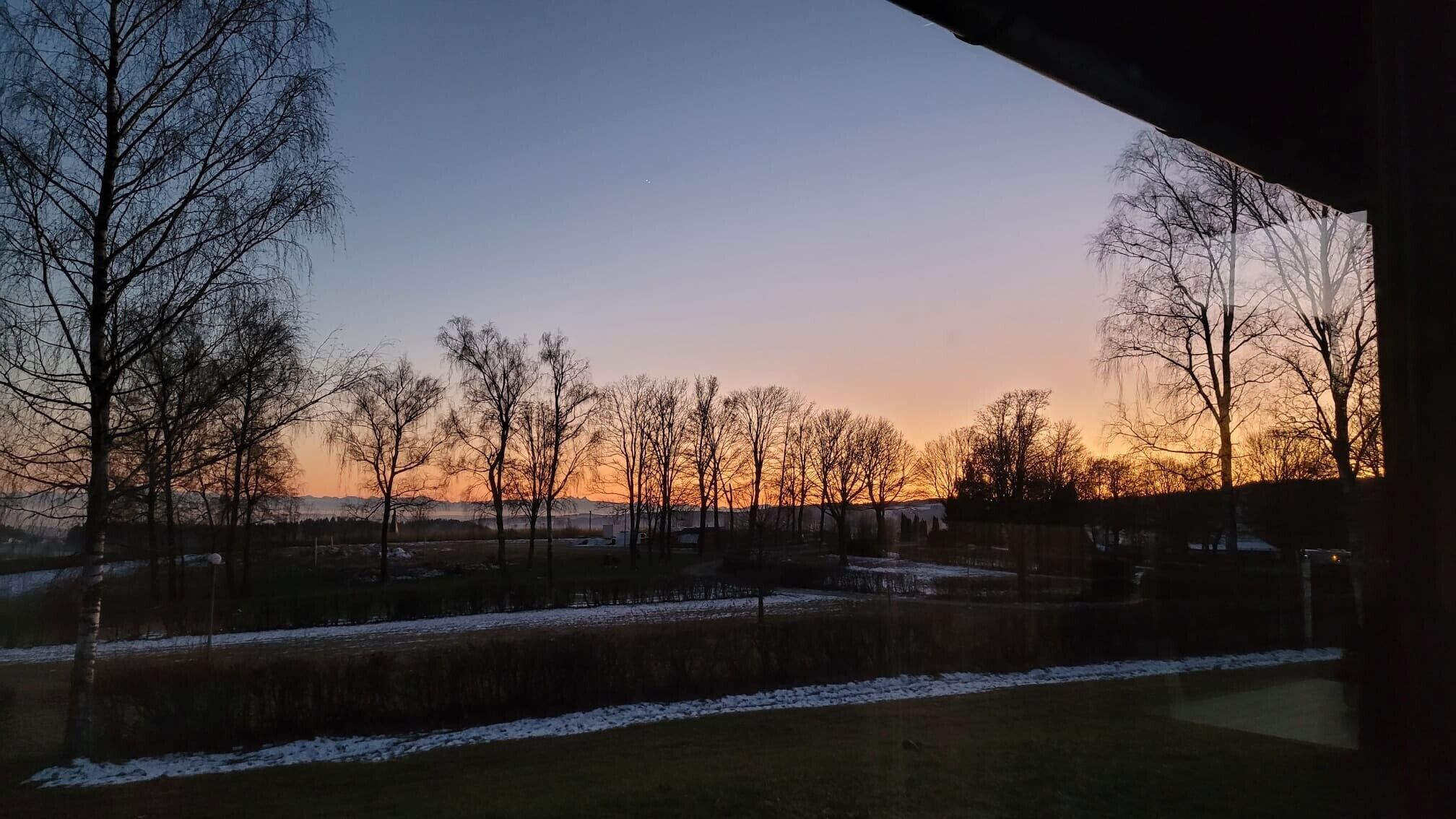 Une vue d’un paysage avec des arbres et une étendue d’eau, probablement un lac ou une rivière, au coucher du soleil.