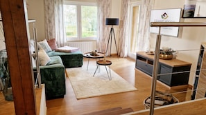 A modern living room with a green sofa, a small round table, a floor lamp, and a view of the outdoors through a window. - Wald Chalet Maxl – Where Time Stands Still and the Soul Finds Peace (Untergriesbach)