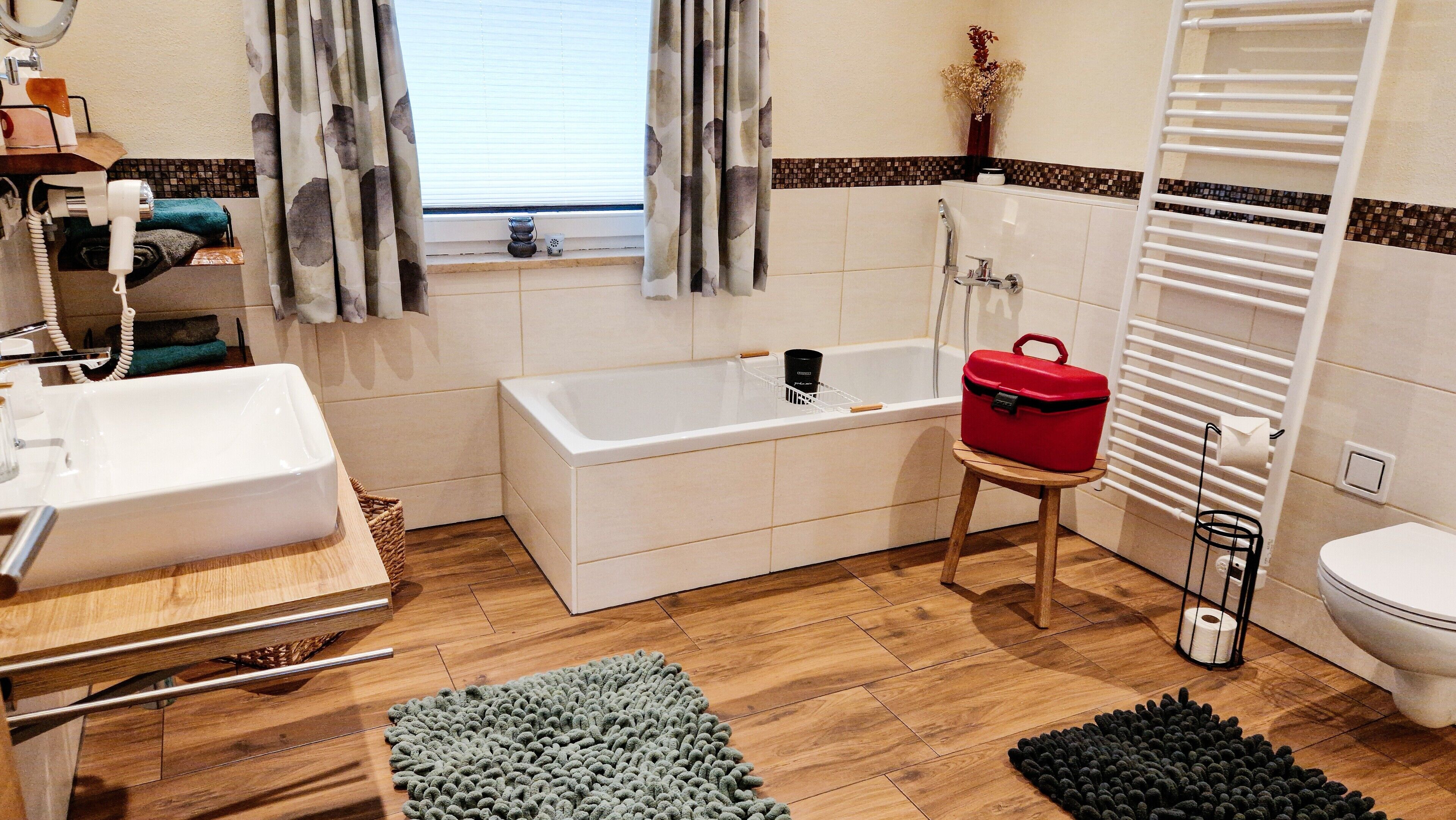 A bathroom with a bathtub, a sink, a toilet, a shower, and a window with curtains.