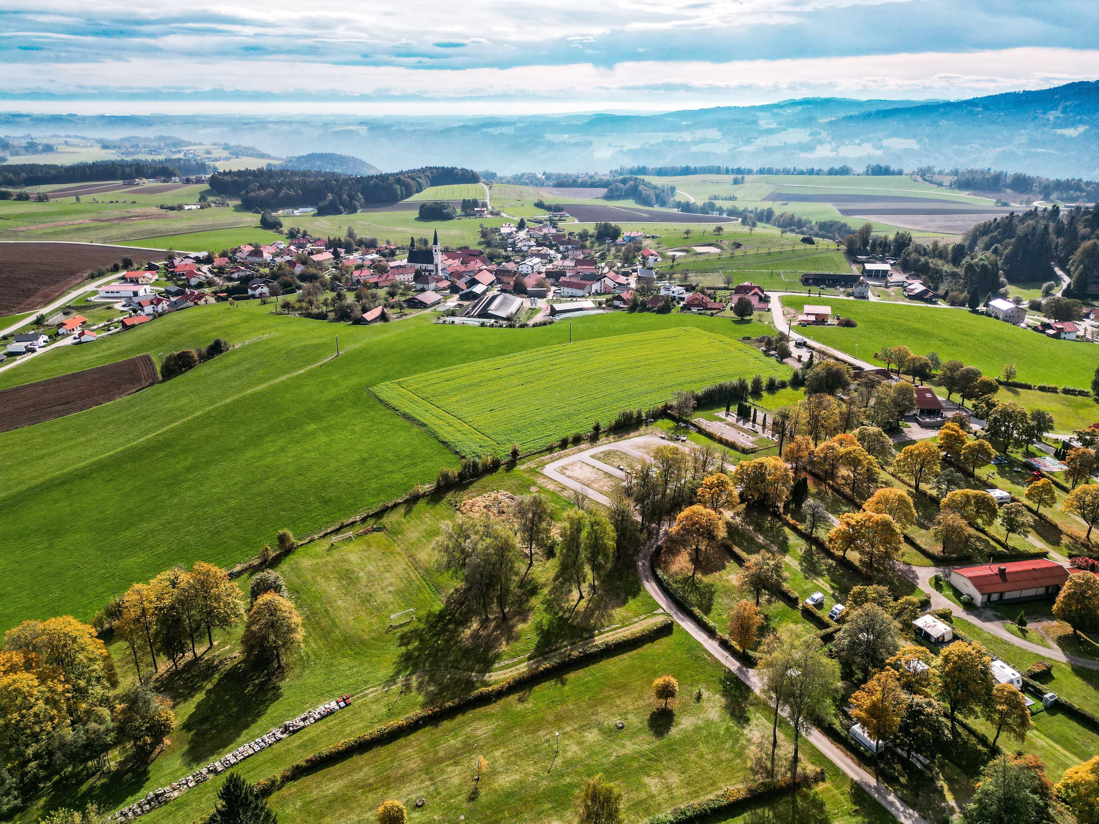 Vista aérea de uma aldeia rural com campos, casas e uma igreja.