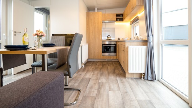 A compact kitchen with wooden cabinets, a built-in oven, and a dining area with a table and chairs. - Tiny Home 'Franzl' with Mountain View, Wi-Fi and Air Conditioning (Untergriesbach)