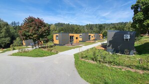 A modern building with a paved driveway, outdoor seating, and a small garden area. - Tiny Home 'Franzl' with Mountain View, Wi-Fi and Air Conditioning (Untergriesbach)
