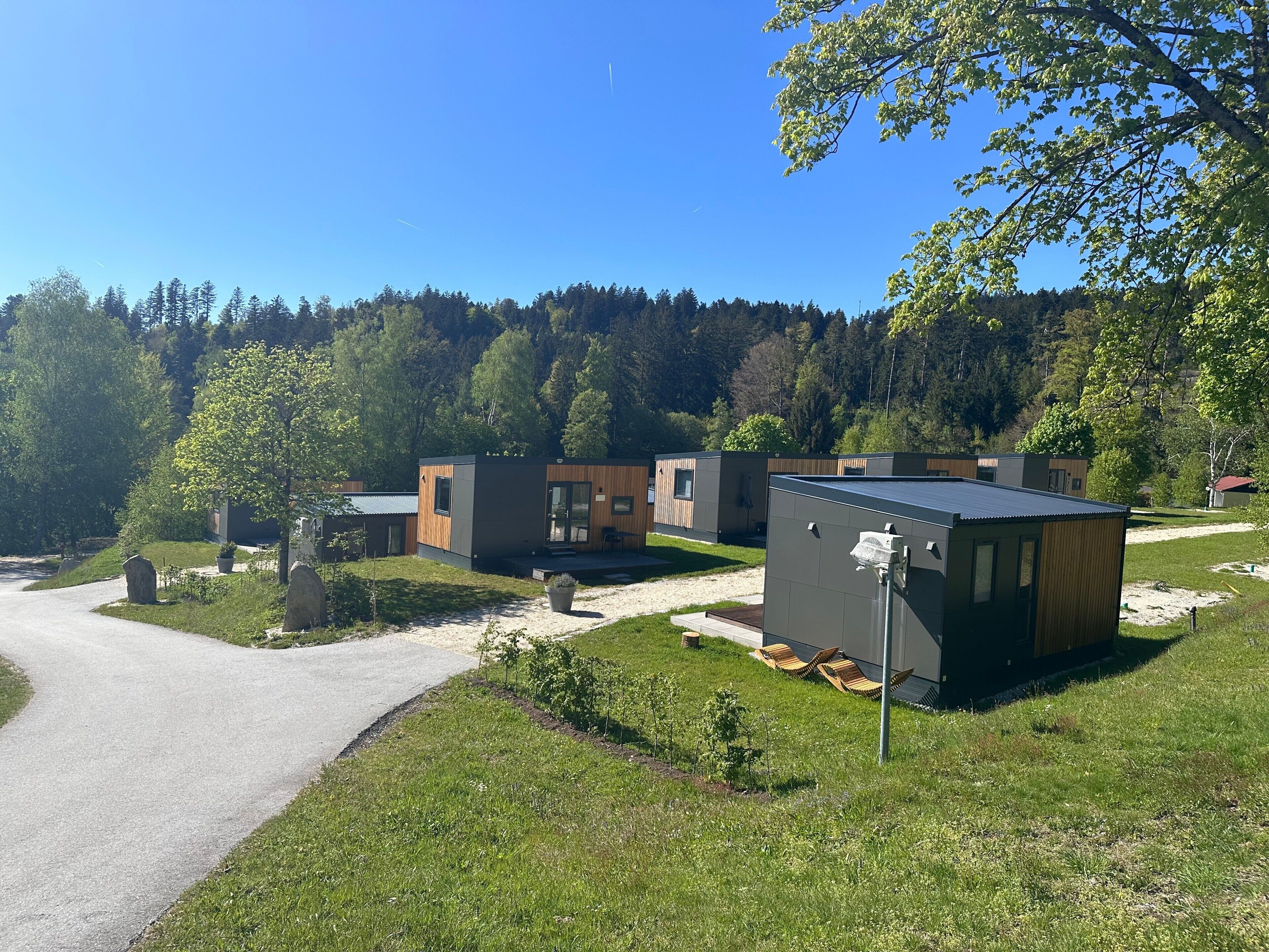 Ein moderner Außenbereich mit einem gepflasterten Weg, Holzbanken und einem kleinen Gebäude mit dunklem Dach.
