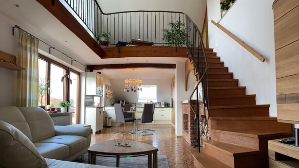 A spacious living area with a high ceiling, a staircase, and a kitchen in the background. - Apartment 'Maisonette Am See' with Lake View, Wi-Fi and Air Conditioning (Nonnenhorn)