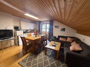 Un espace de vie chaleureux comprenant une table à manger, des chaises, un canapé, un téléviseur et, au fond, une cuisine.