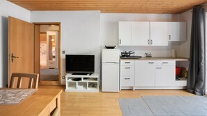 A compact kitchen with white cabinets, a refrigerator, a TV, and a dining area with a table and chairs. - Apartment 'Village Idyll' with Balcony and Wi-Fi in the Picturesque Countryside of Jesenwang (Jesenwang)