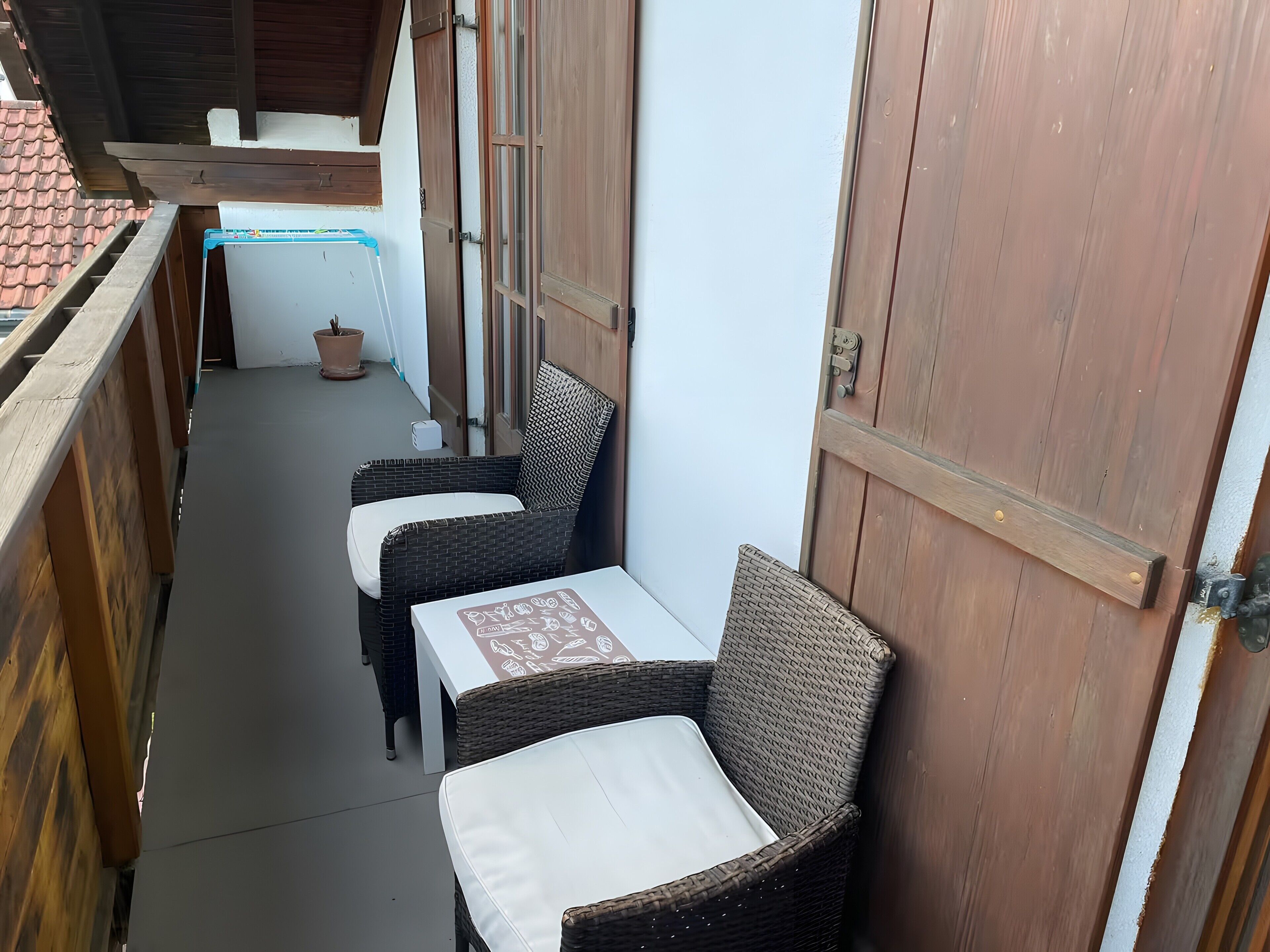 Ein schmaler Balkon im Freien mit Korbmöbeln und einer Holztür.