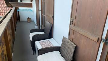 Ein schmaler Balkon im Freien mit Korbmöbeln und einer Holztür.