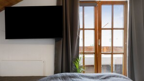 A bedroom with a bed, a TV mounted on the wall, a window with curtains, and a radiator. - Apartment 'Village Idyll' with Balcony and Wi-Fi in the Picturesque Countryside of Jesenwang (Jesenwang)