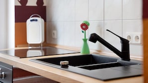 A modern kitchen with a black faucet, a green vase with a red flower, and a white appliance on the counter. - Apartment 'Meer-Natur-Idyll' with Wi-Fi (Peenemünde)
